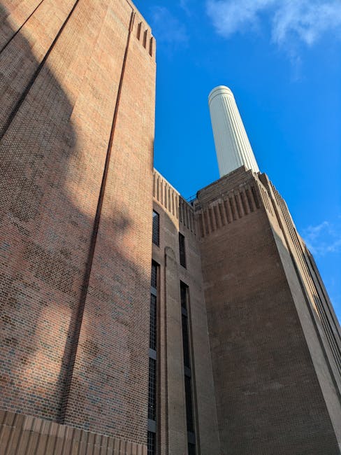The image features the iconic Battersea Power Station with its distinctive brick facade and tall chimney rising against a bright blue sky with scattered white clouds. The perspective is from the groun
