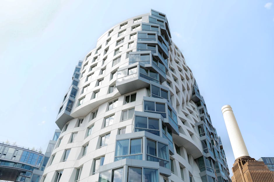 A modern, multi-story residential building with a curvilinear architectural design, featuring numerous large, rectangular windows that project outward in varying angles. The facade is predominantly wh